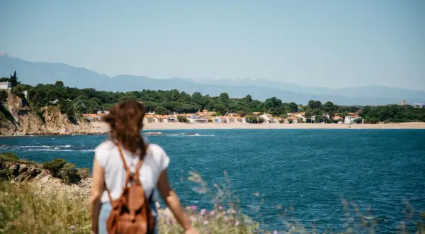 Vue sur la mer et des maisons colorées, une femme avec un sac à dos profite d'une belle randonnée.