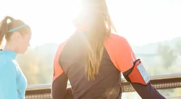 Deux femmes s'entraînent dehors, profitant du soleil. L'une porte un brassard pour son téléphone, prête à courir sous 30 degrés.