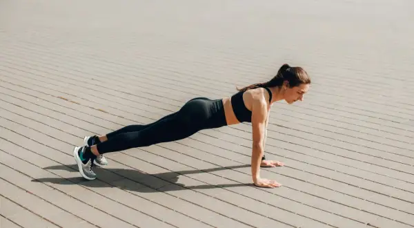 Femme en tenue de sport faisant une planche sur un sol pavé. Elle est concentrée, le corps gainé. Quel est le meilleur sport ? Celui qui vous fait vous sentir ainsi !