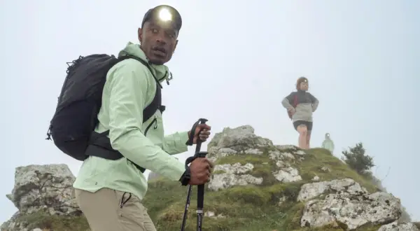 Randonneur ajustant le réglage de ses bâtons de marche sur un sentier brumeux. D'autres randonneurs sont visibles en arrière-plan.