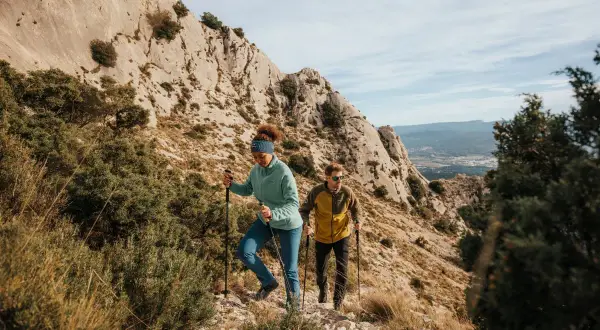 Deux randonneurs font du fast hiking sur un sentier rocailleux, profitant d'un paysage montagneux spectaculaire.
