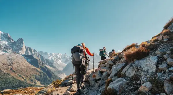 Randonneurs sur un sentier rocheux, le Tour du Mont Blanc difficulté est palpable. Paysage alpin grandiose sous un ciel bleu.