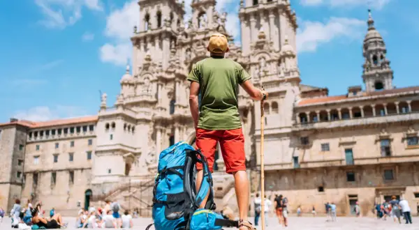 Pèlerin du **marche saint jacques de compostelle** contemplant la cathédrale. Sac à dos bleu et bâton de marche à ses côtés.