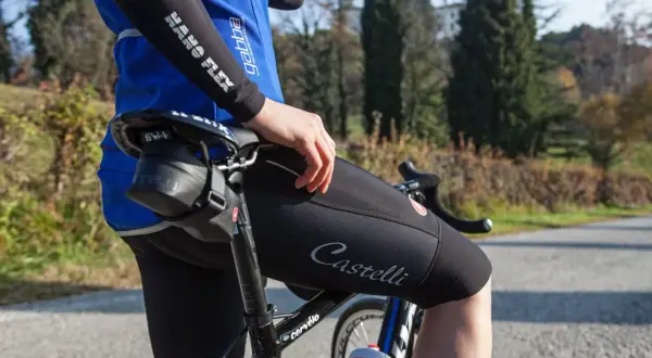 Cycliste ajustant le réglage inclinaison selle vélo route. Vêtement Castelli, maillot bleu, cuissard noir.