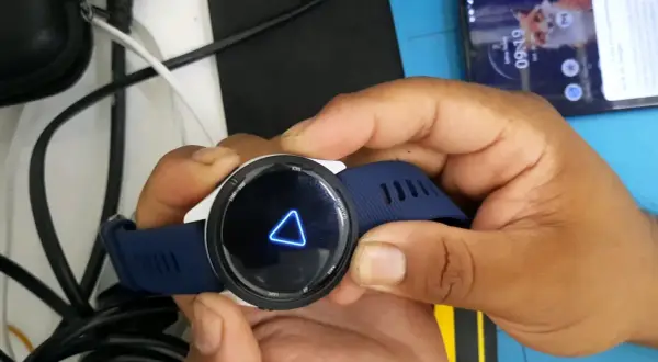 Montre Garmin avec un triangle bleu lumineux sur l'écran. La montre est tenue par des mains.