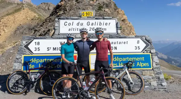 Trois cyclistes posent fièrement devant le panneau du Col du Galibier, altitude 2645m, après une ascension difficile.