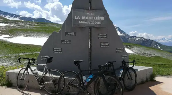 Trois vélos de route devant le monument du col de la Madeleine, une carte des altitudes des villages environnants.