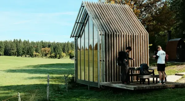 Deux randonneurs s'arrêtent près d'une cabane moderne, planifiant leur rando Jura 2 jours boucle.