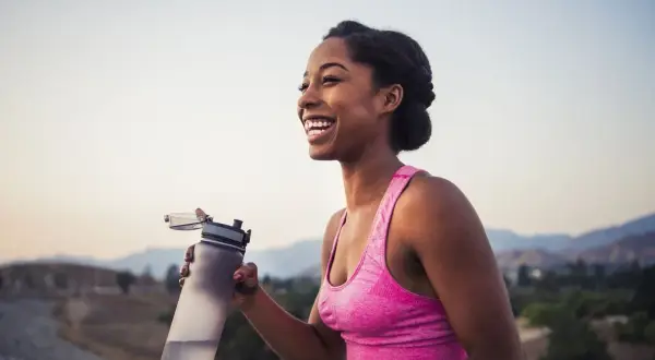 Une femme souriante tient une bouteille d'eau après son entraînement. Le sport est essentiel pour la perte de poids et le bien-être.