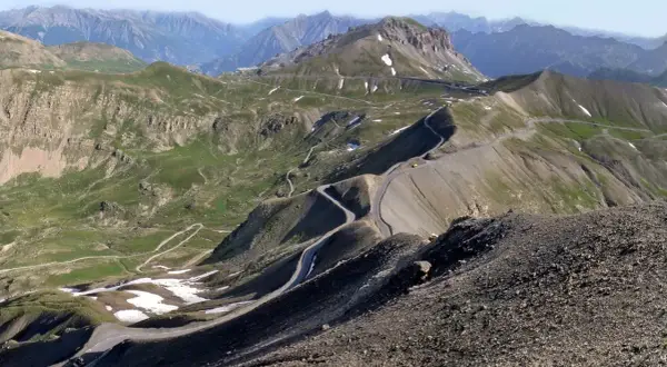 Vue panoramique du col de la Bonette, avec sa route sinueuse traversant des paysages montagneux verdoyants et rocailleux.
