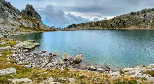 Lac de montagne aux eaux bleues, entouré de rochers et d'herbes sèches. Un paysage sauvage, peut-être une randonnée de gr 52 difficulté.