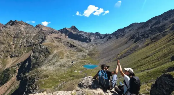 Deux randonneurs célèbrent leur succès au sommet, avec un lac bleu et des montagnes majestueuses en arrière-plan. Une parfaite randonnée à Aoste.