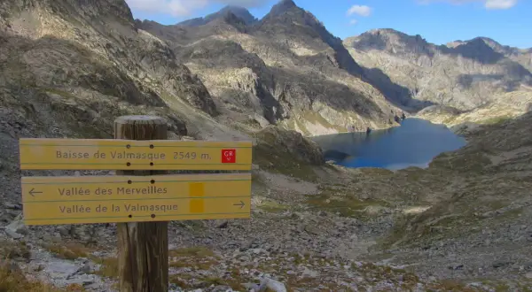 Panneau indicateur pour la randonnée vallée des Merveilles 2 jours. Lac d'altitude et montagnes escarpées.