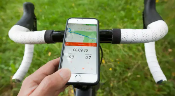 Un cycliste utilise son smartphone avec une application type komoot ou Strava pour suivre sa sortie. La carte et les stats sont visibles.