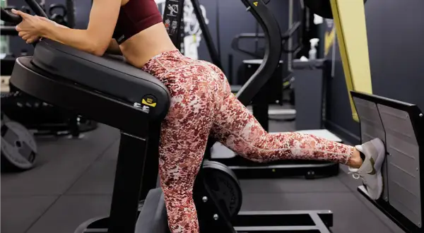 Femme effectuant un exercice fessier sur une machine de musculation, concentrée sur le renforcement de ses muscles.