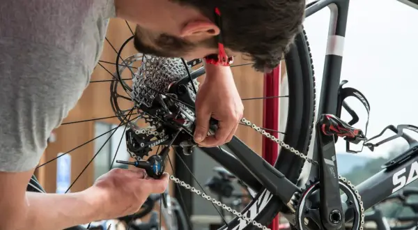 Un mécanicien ajuste le **réglage du dérailleur arrière** d'un vélo de course avec un outil Allen.