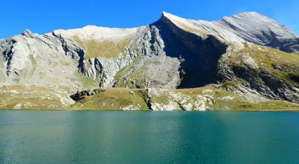 Lac d'altitude aux eaux turquoise, bordé de montagnes rocheuses et herbeuses. Un paysage qui évoque la beauté sauvage du tour du Queyras, mais aussi sa difficulté.
