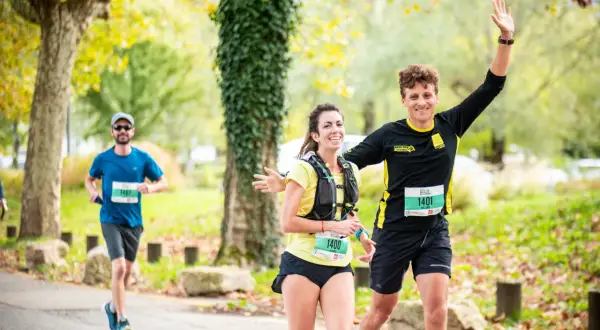 Coureurs souriants lors d'une course, un homme agite la main. Idéal pour un plan entraînement semi-marathon débutant.
