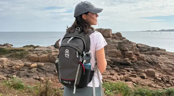 Jeune femme avec un sac à dos, prête à faire de la randonnée sur un sentier côtier rocheux, face à la mer.