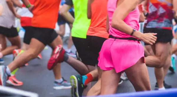Des coureurs en tenues vives s'élancent sur la piste mouillée. L'un d'eux, en rose vif, semble vivre son premier marathon, déterminé.