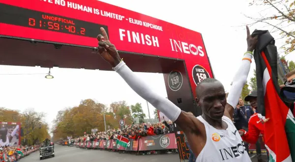 Eliud Kipchoge franchit la ligne d'arrivée, record marathon homme officiellement battu. Il brandit le drapeau kenyan, célébrant son exploit.