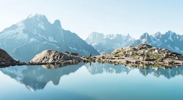 Un lac alpin reflète des montagnes majestueuses. Une randonneuse admire le paysage, un aperçu des meilleures randonnées en France.