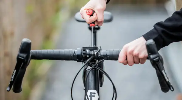 Ajustement du guidon de vélo avec un tournevis. Les mains manipulent la potence pour remonter le guidon vélo.