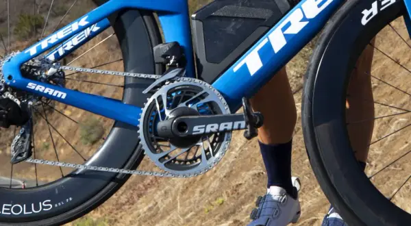 Démonter pédale vélo : gros plan sur le pédalier SRAM d'un vélo de course Trek bleu, avec une jambe de cycliste en chaussures blanches.