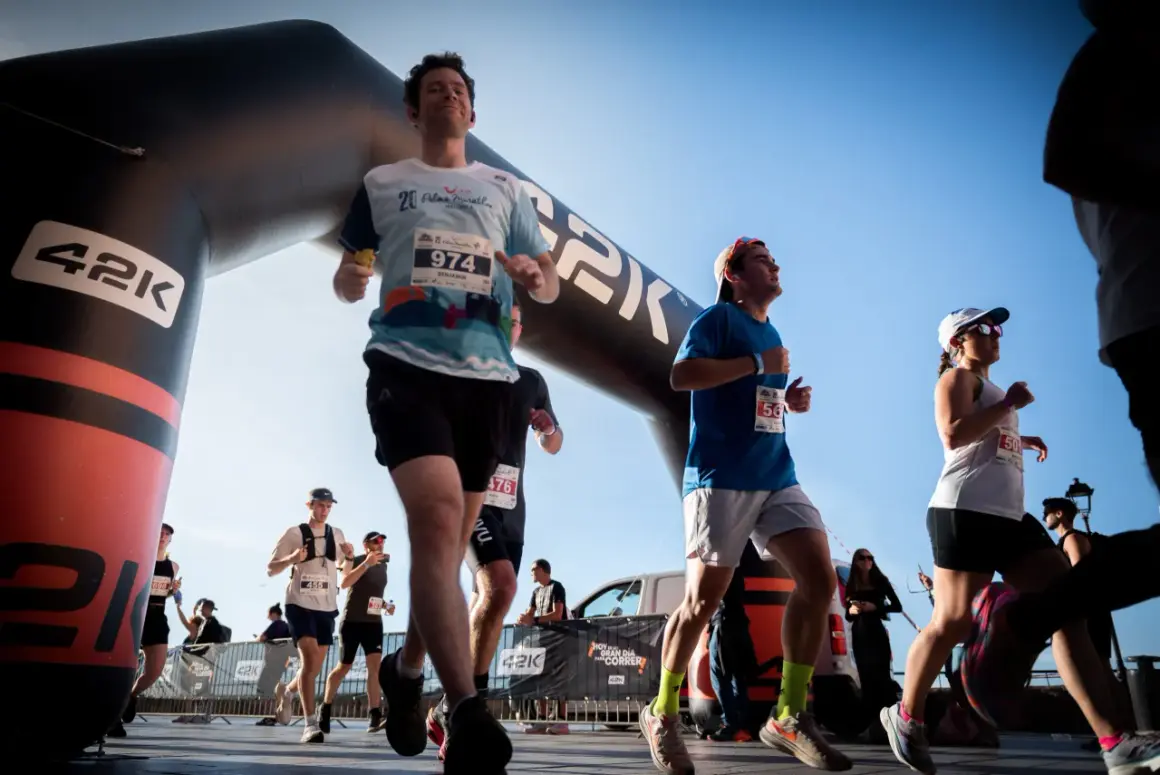 Des coureurs franchissent une arche de départ, prêts à se préparer pour le semi-marathon. Le soleil brille sur la course.