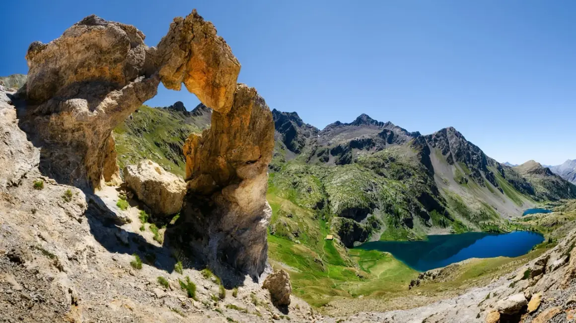 Un arc rocheux spectaculaire domine un paysage de montagne verdoyant avec des lacs bleus, une vue typique du tour du Mercantour.