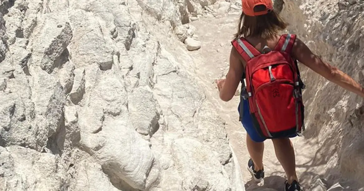 Randonneuse avec sac à dos rouge sur un sentier rocailleux, tout l'équipement nécessaire pour le GR20.