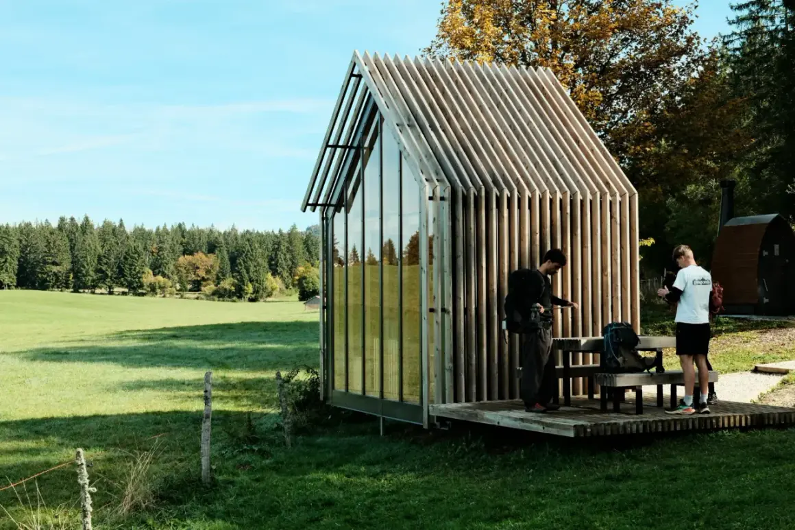 Deux randonneurs s'arrêtent près d'une cabane moderne, planifiant leur rando Jura 2 jours boucle.