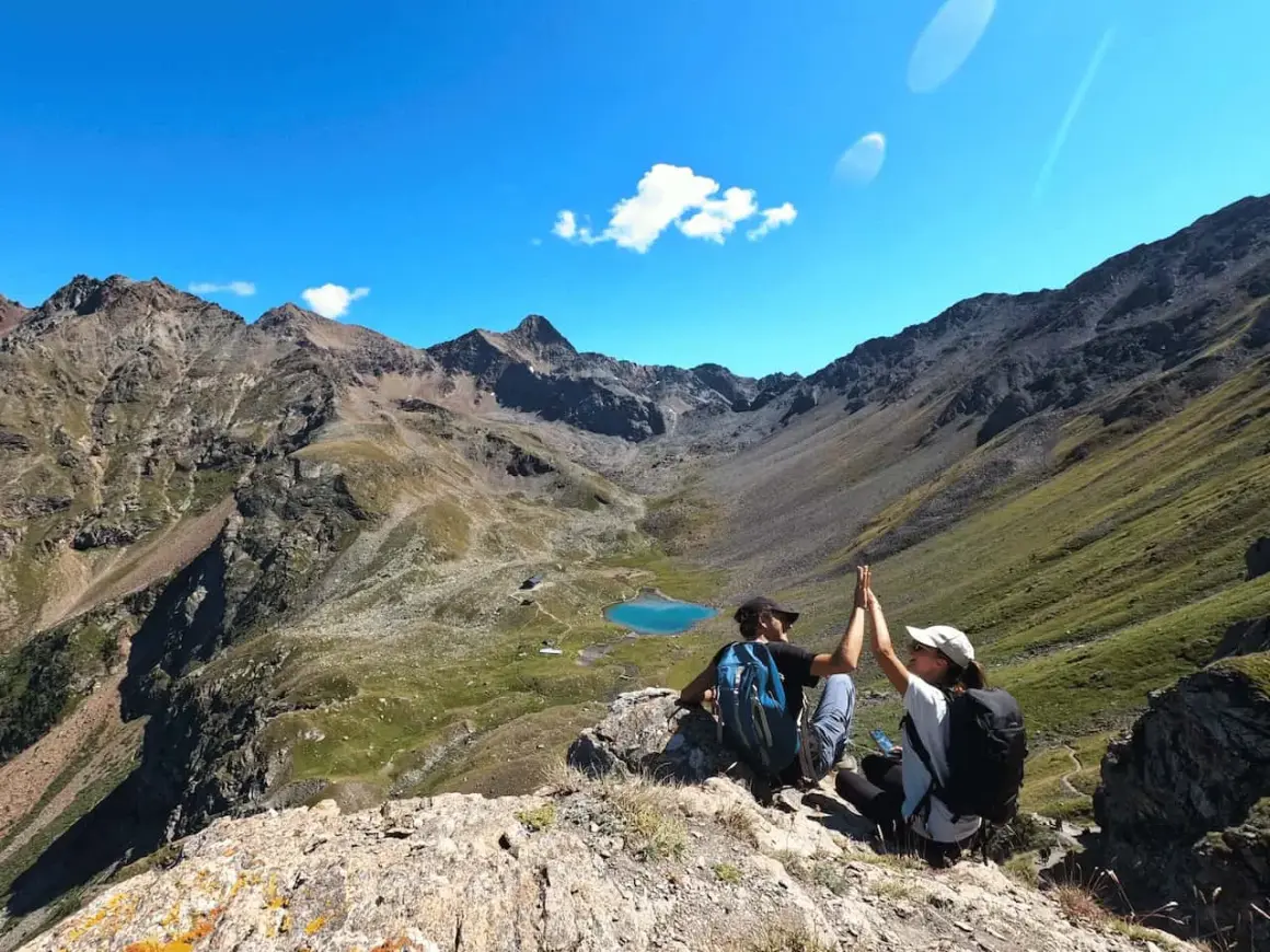 Deux randonneurs célèbrent leur succès au sommet, avec un lac bleu et des montagnes majestueuses en arrière-plan. Une parfaite randonnée à Aoste.
