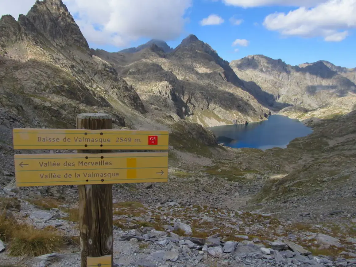 Panneau indicateur pour la randonnée vallée des Merveilles 2 jours. Lac d'altitude et montagnes escarpées.