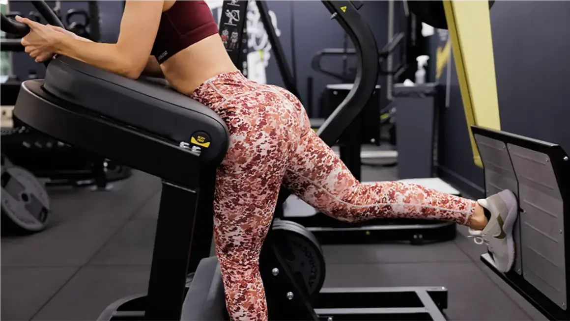 Femme effectuant un exercice fessier sur une machine de musculation, concentrée sur le renforcement de ses muscles.