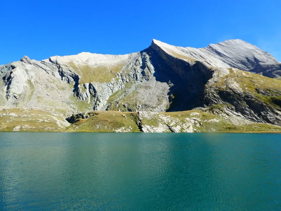 Lac d'altitude aux eaux turquoise, bordé de montagnes rocheuses et herbeuses. Un paysage qui évoque la beauté sauvage du tour du Queyras, mais aussi sa difficulté.