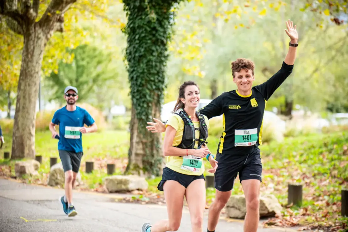 Coureurs souriants lors d'une course, un homme agite la main. Idéal pour un plan entraînement semi-marathon débutant.