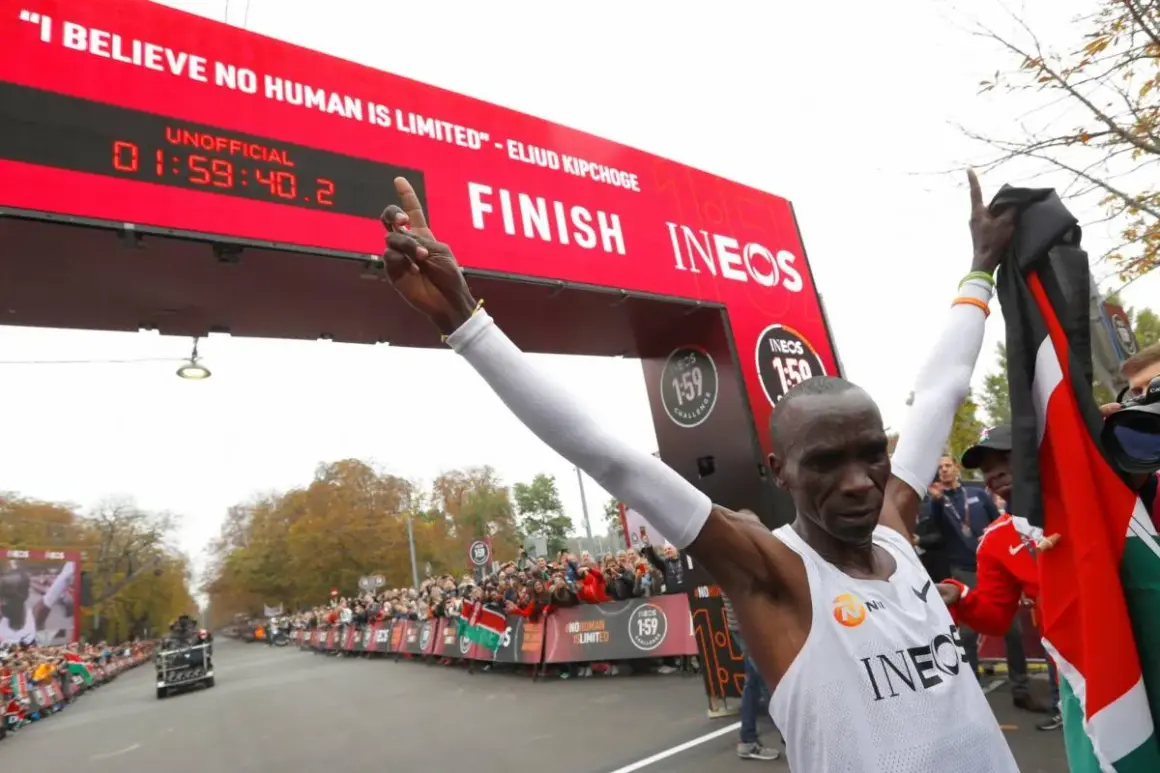 Eliud Kipchoge franchit la ligne d'arrivée, record marathon homme officiellement battu. Il brandit le drapeau kenyan, célébrant son exploit.
