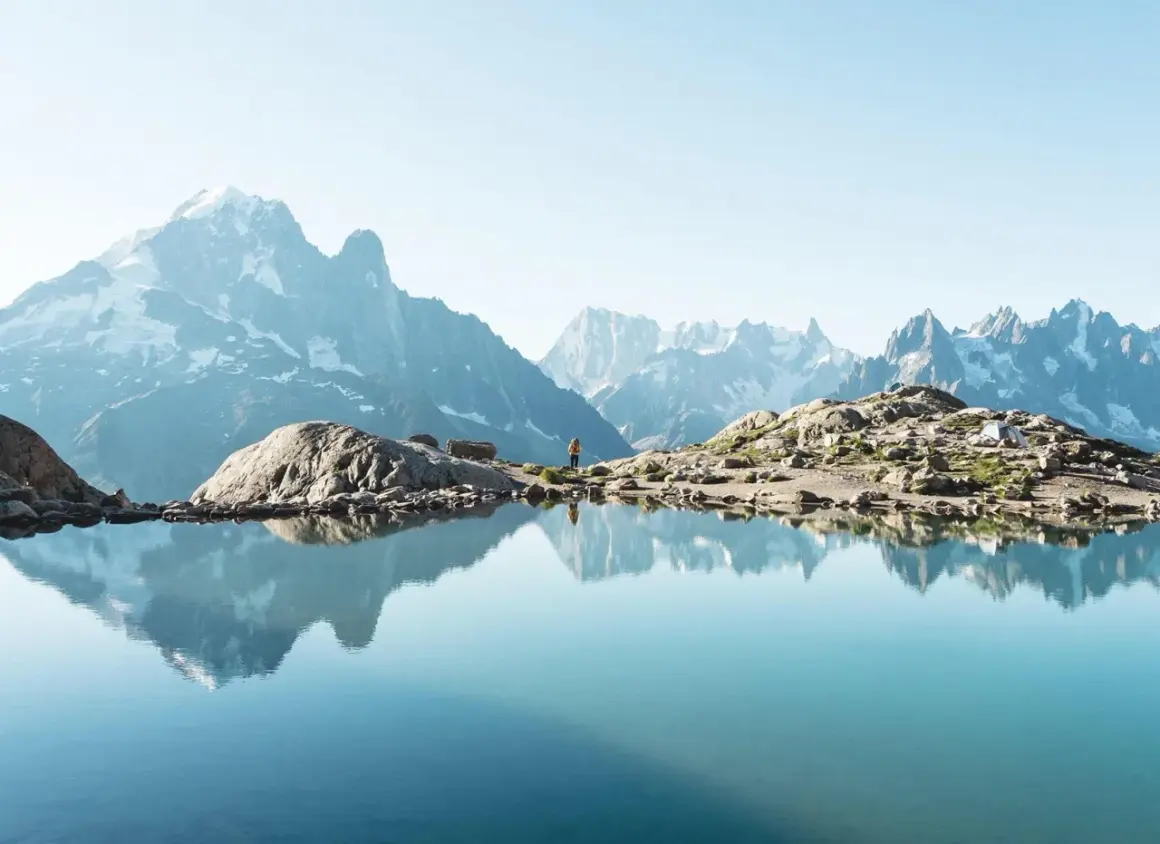 Un lac alpin reflète des montagnes majestueuses. Une randonneuse admire le paysage, un aperçu des meilleures randonnées en France.