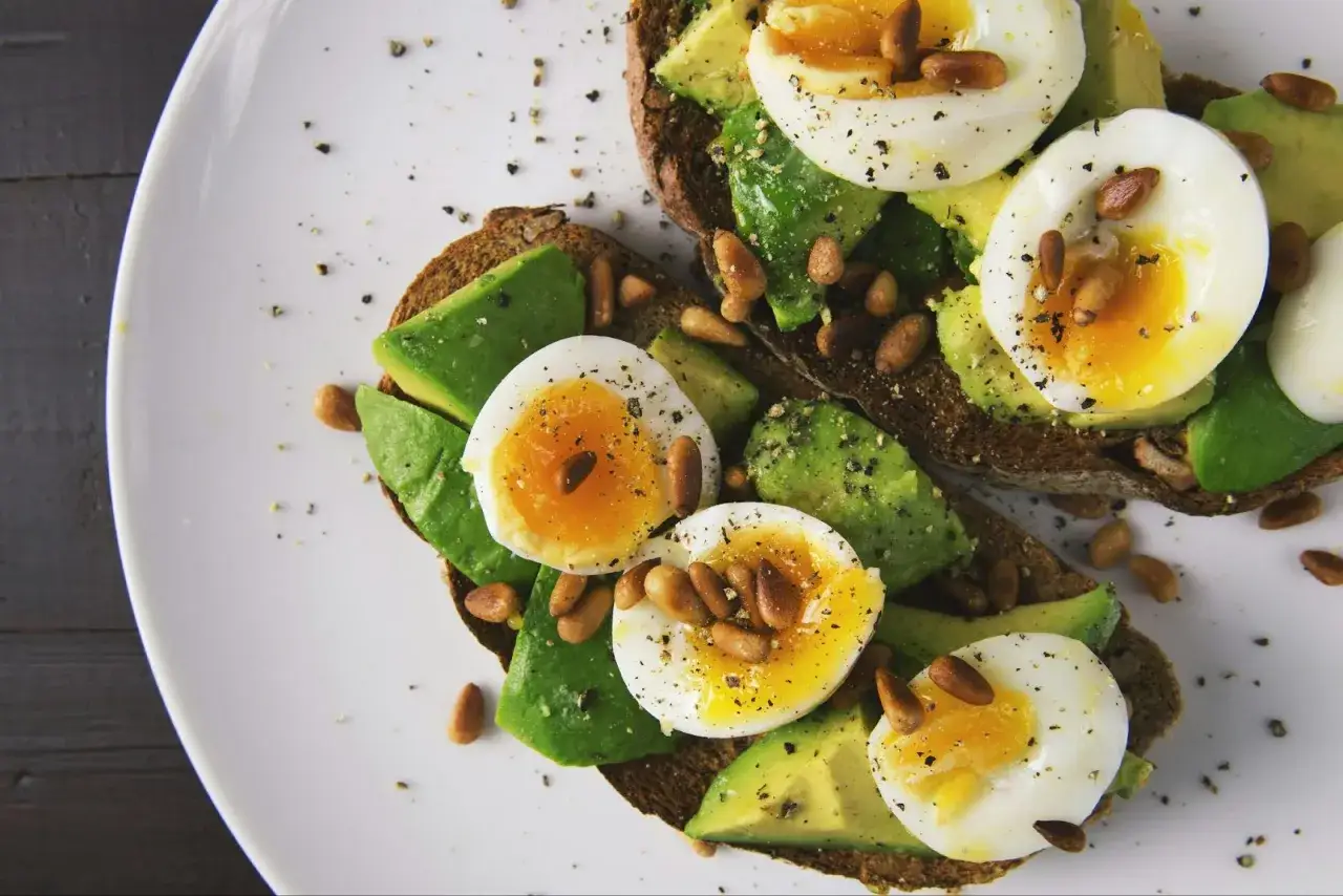 Quel petit déjeuner avant sport : toasts de pain complet avec avocat, œufs mollets, pignons de pin et poivre.