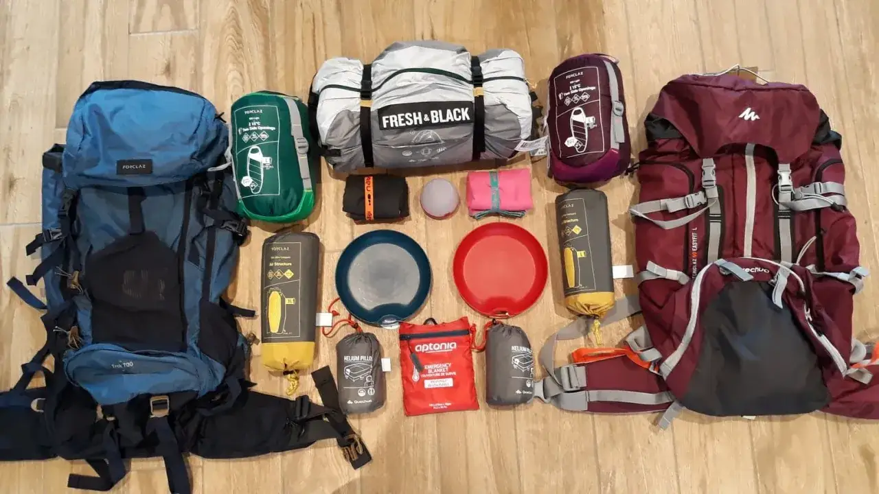 Checklist camping : sacs à dos, sacs de couchage, matelas, assiettes, lampe et couverture de survie. Tout le nécessaire pour une aventure en plein air.