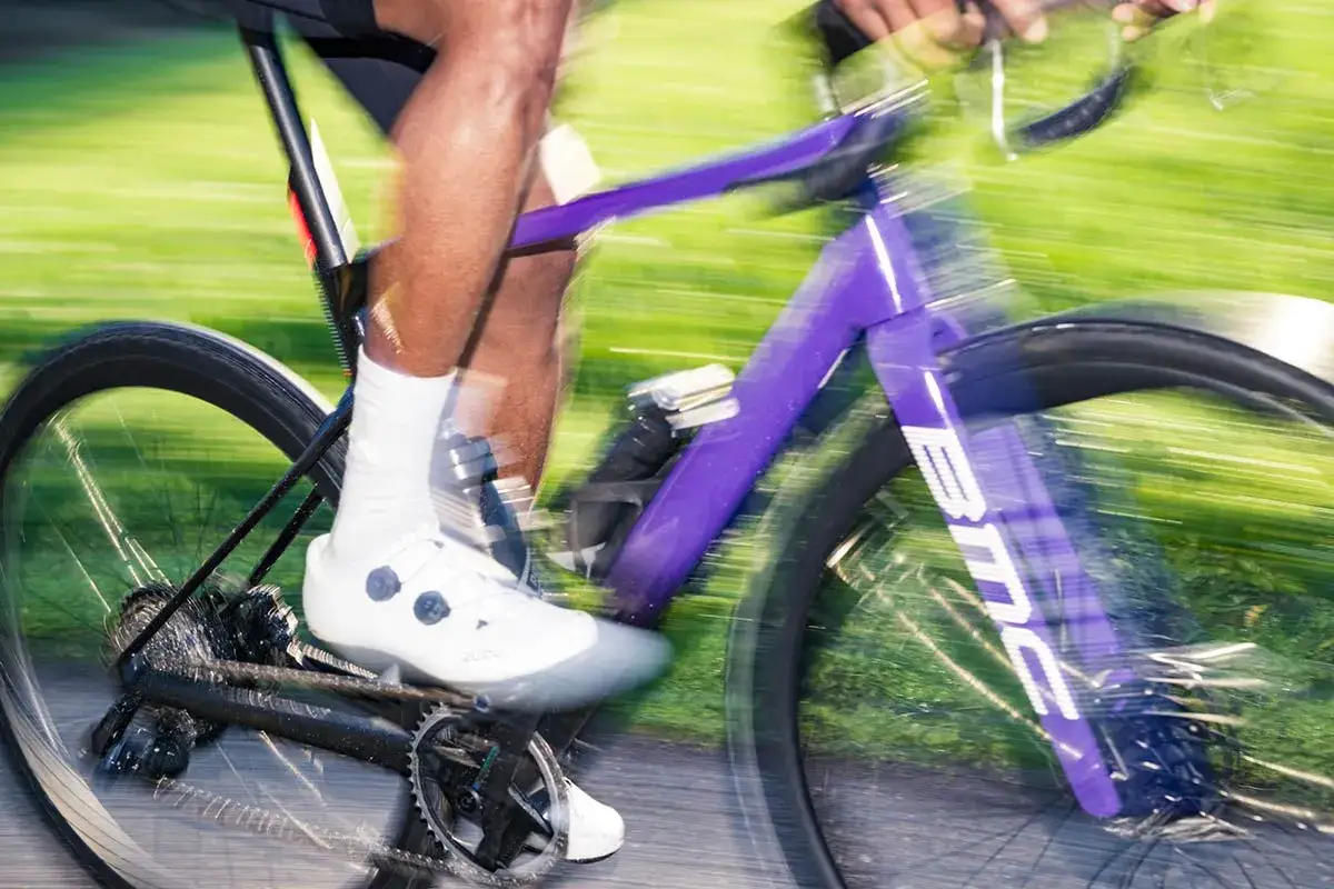 Un cycliste en tenue blanche commence le v&eacute;lo de route sur un v&eacute;lo violet vif, le mouvement flou sugg&eacute;rant la vitesse.