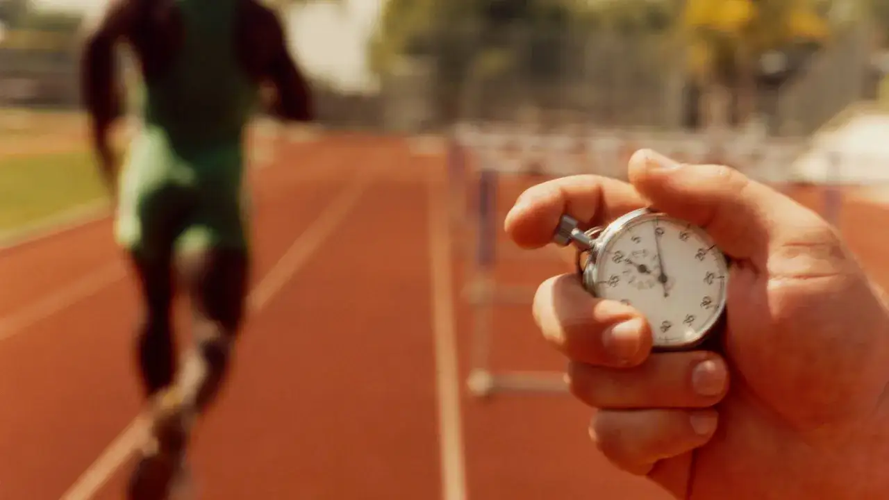 Chronomètre en main, prêt à chronométrer un athlète en plein entraînement fractionné sur la piste.