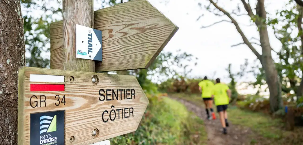 Panneaux indicateurs pour un sentier c&ocirc;tier GR 34 en Bretagne, avec deux coureurs en arri&egrave;re-plan.