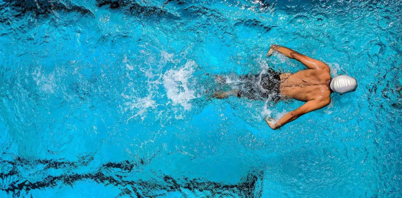 Un nageur en plein effort, peut-être se demandant quel est le sport le plus complet. L'eau bleue tourbillonne autour de lui.