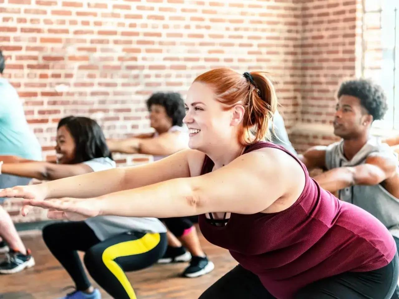 Groupe diversifi&eacute; en plein cours de fitness, pratiquant des squats pour le sport perte de poids. Sourires et d&eacute;termination sur les visages.