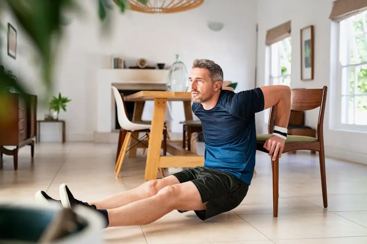 Un homme fait des dips sur une chaise &agrave; la maison, une belle illustration de la sport motivation pour rester en forme.