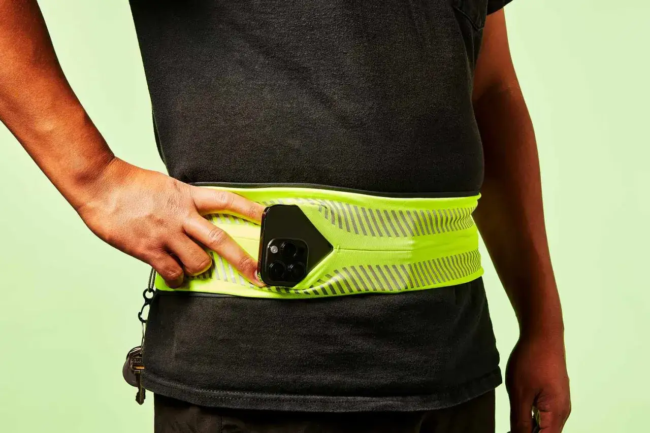 Ceinture de course fluo pour savoir o&ugrave; mettre son t&eacute;l&eacute;phone quand on court. Une main ins&egrave;re un smartphone dans la poche.