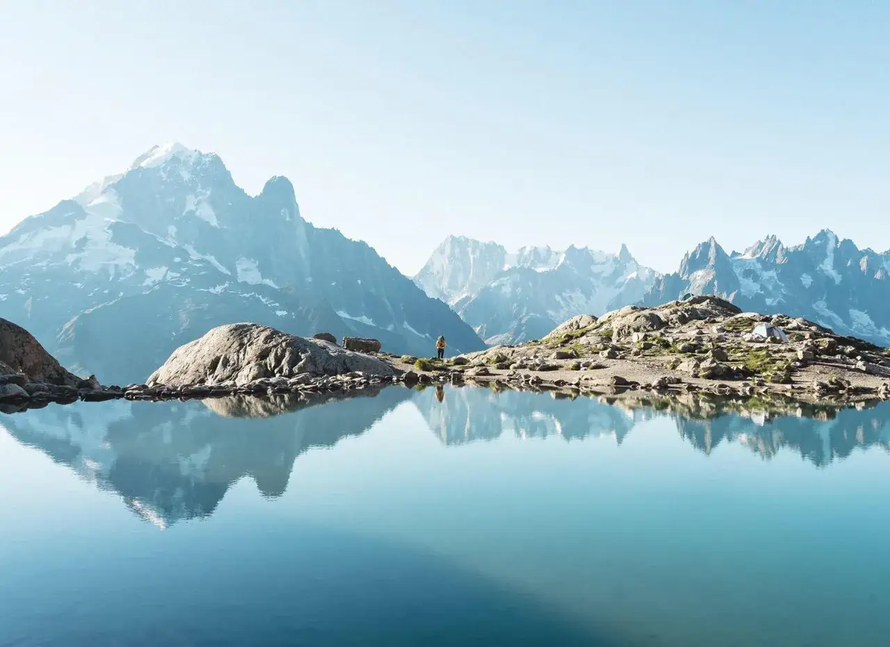 Une personne admire un lac alpin paisible refl&eacute;tant des montagnes enneig&eacute;es. Une belle randonn&eacute;e dans un paysage spectaculaire.