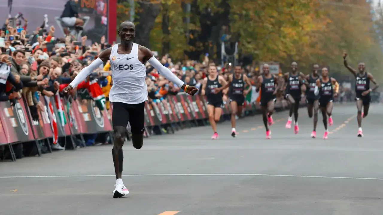 Un homme franchit la ligne d'arrivée d'un marathon, le sourire aux lèvres, acclamé par la foule. Il est en tête de la course, un record marathon homme en vue.